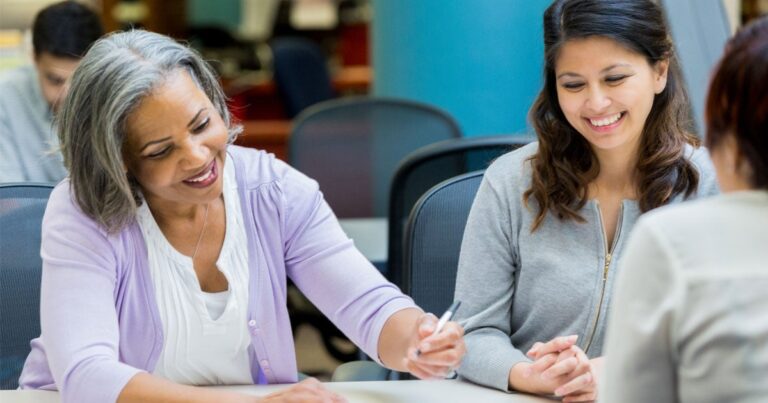 Two women sitting at a table and smiling.